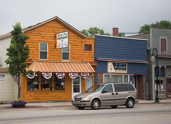 Small town street with wooden building and parked car.