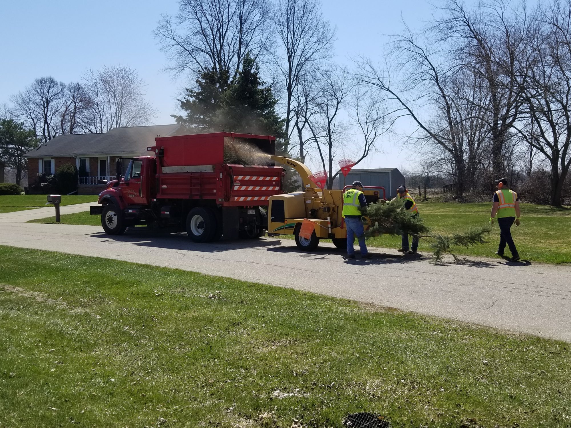 Workers feeding branches into wood chipper truck.