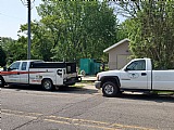 Utility trucks parked roadside near greenery.