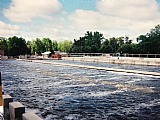 Rushing river with trees and dam in the background.