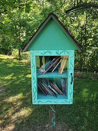 Little free library in green forest setting.